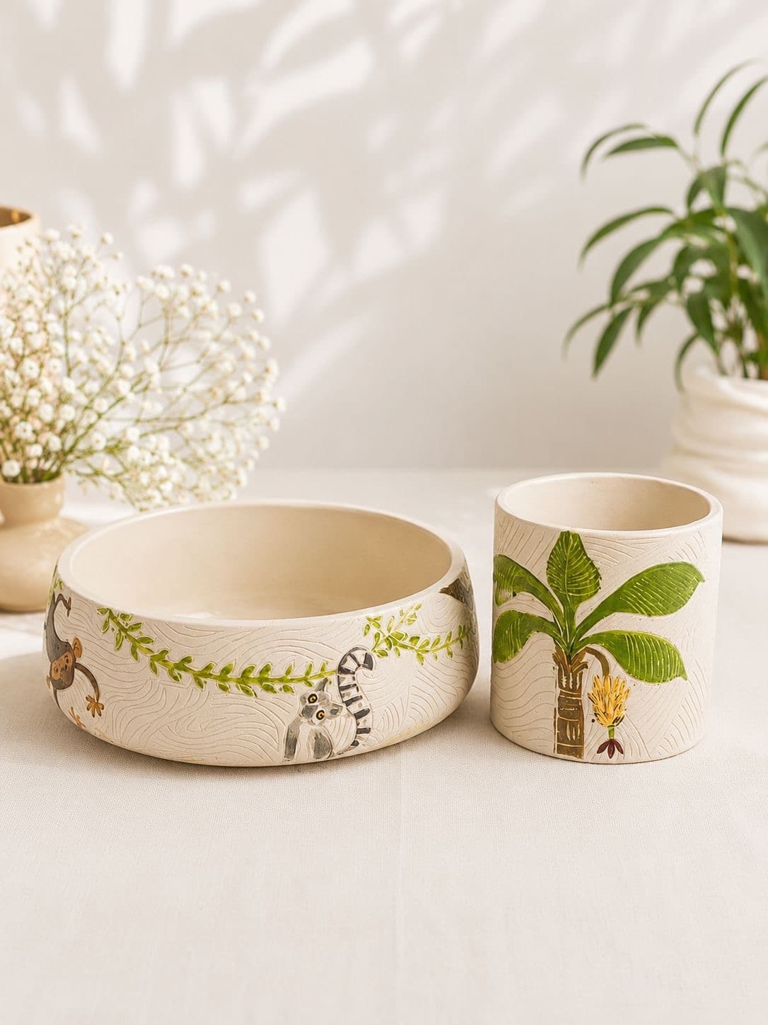 Carved bowl planter painted with a monkey and a ring-tailed lemur beside a cylinder pot painted with a banana palm