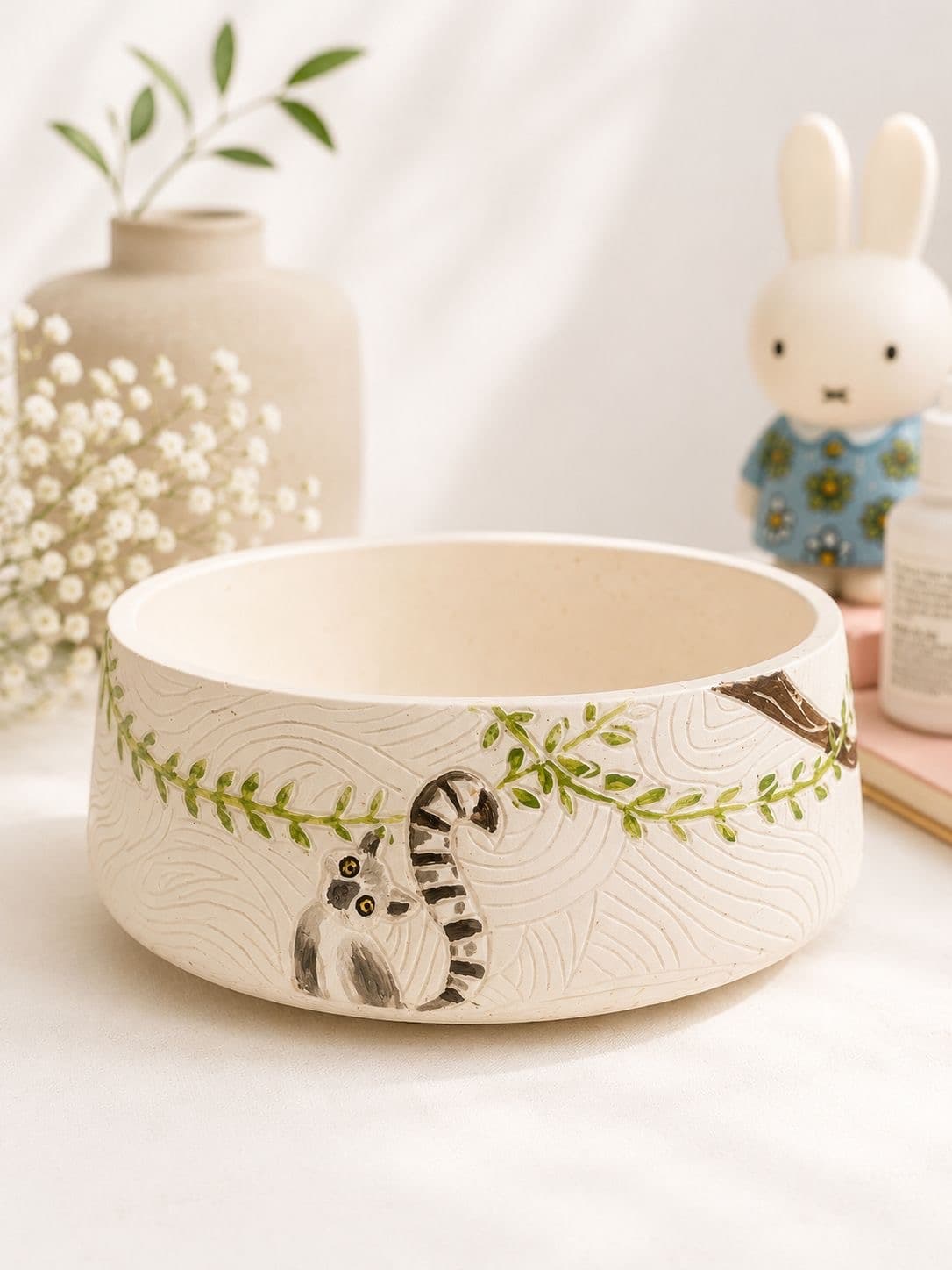 Close-up of the carved wavy sgraffito texture on a bowl planter, with a painted ring-tailed lemur and a trailing vine